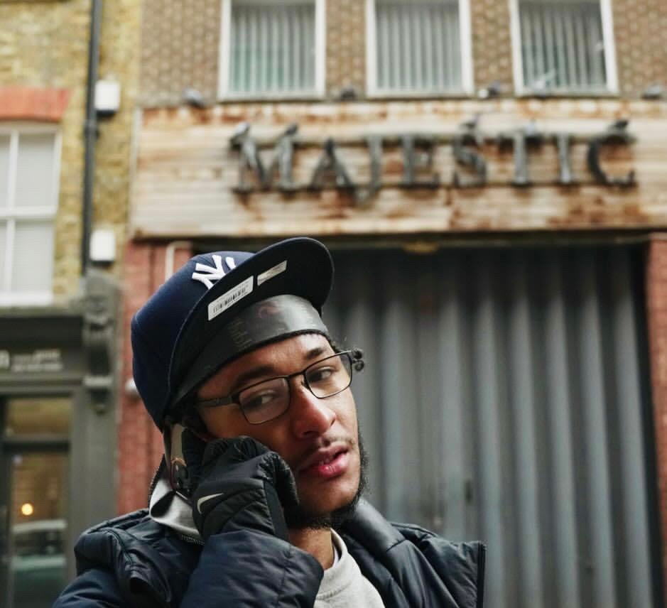 Squintz wearing a NY cap and glasses on an urban street